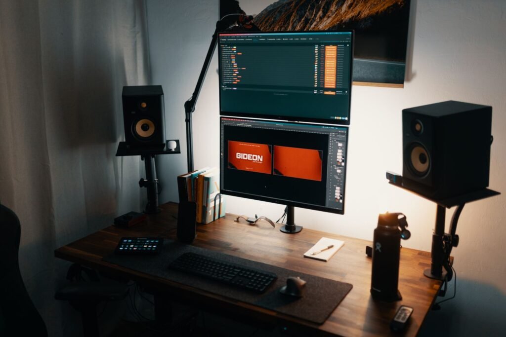 Home studio desk with computer screens and a pair of speakers