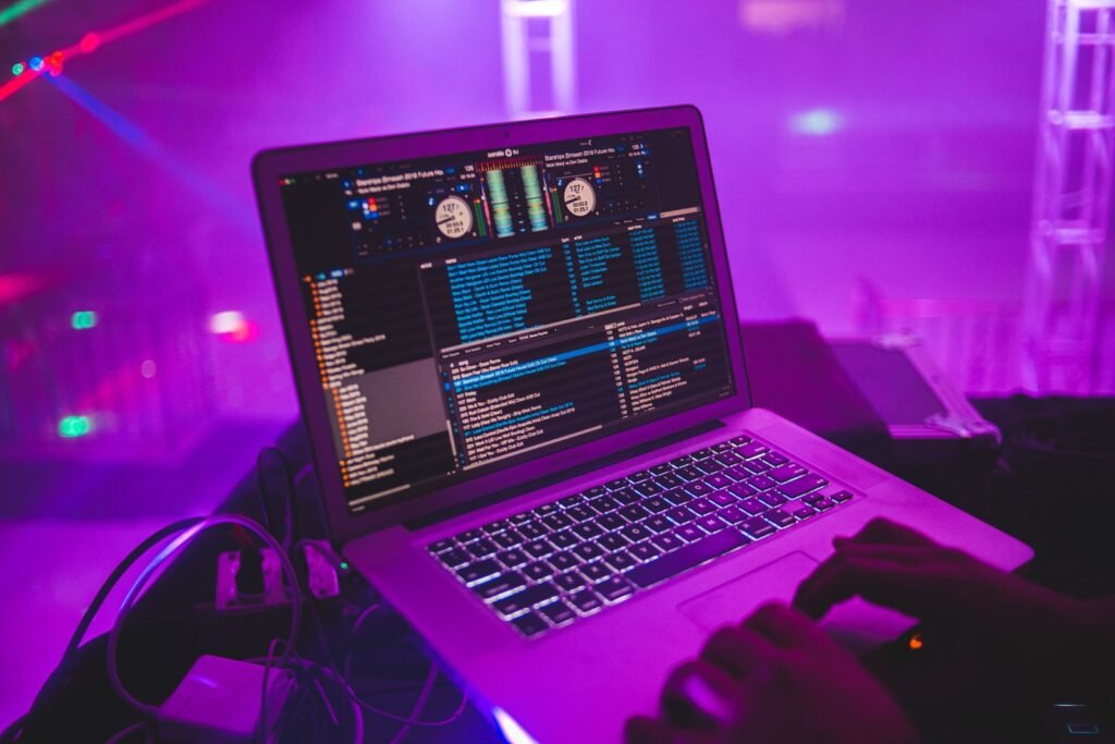 DJ mixing on a laptop with DJ software in a neon-lit club